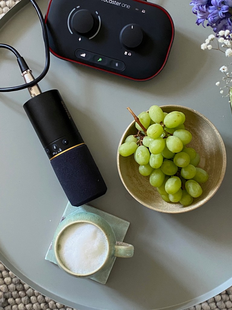 Ein Tisch, auf dem eine Schüssel mit Weintrauben steht, ein Podcast-Mikro liegt und eine Tasse mit Matcha-Latte 